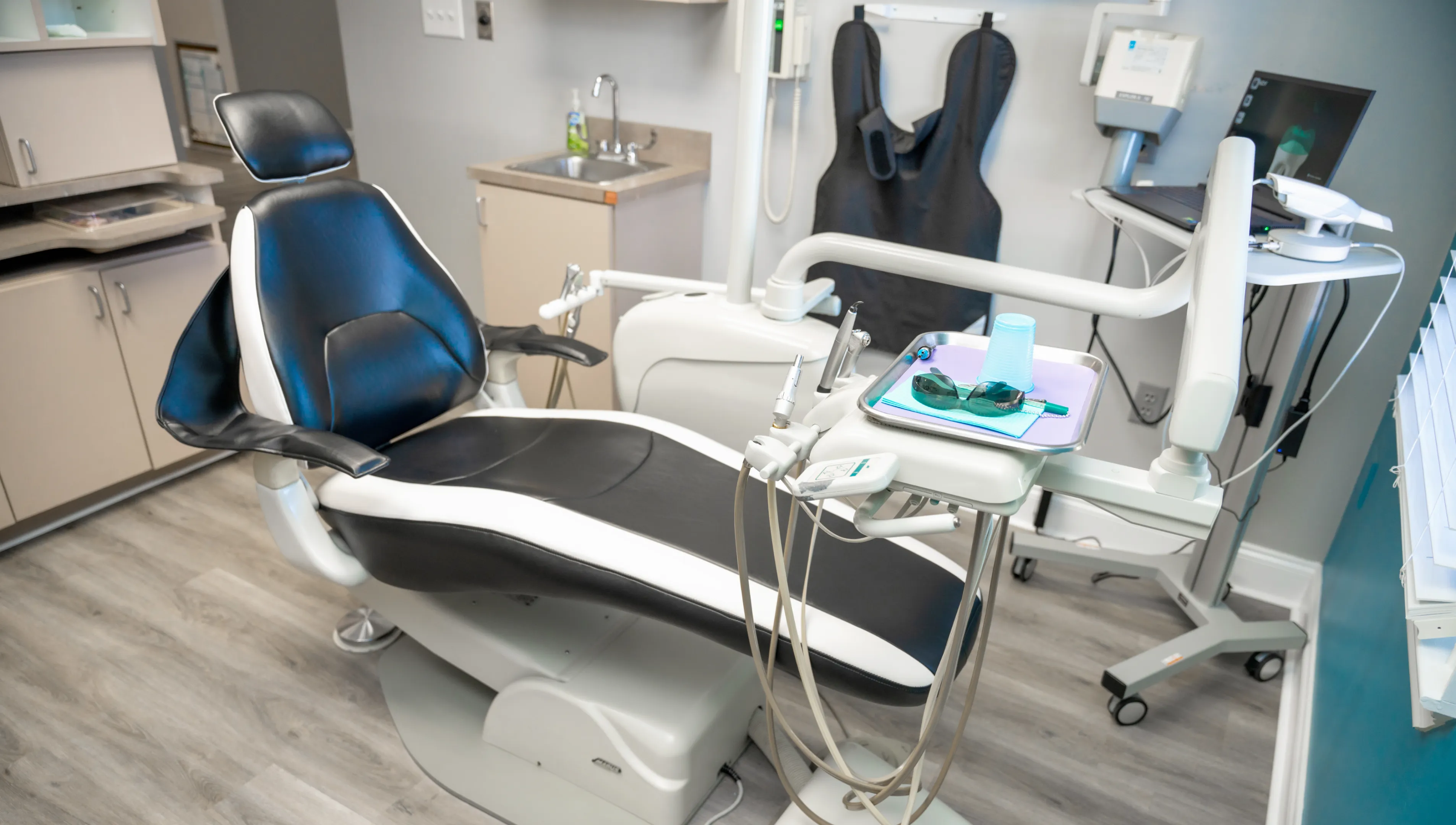 Dental office featuring a black and white dental chair with attached instruments and a tray holding protective glasses and a plastic cup.